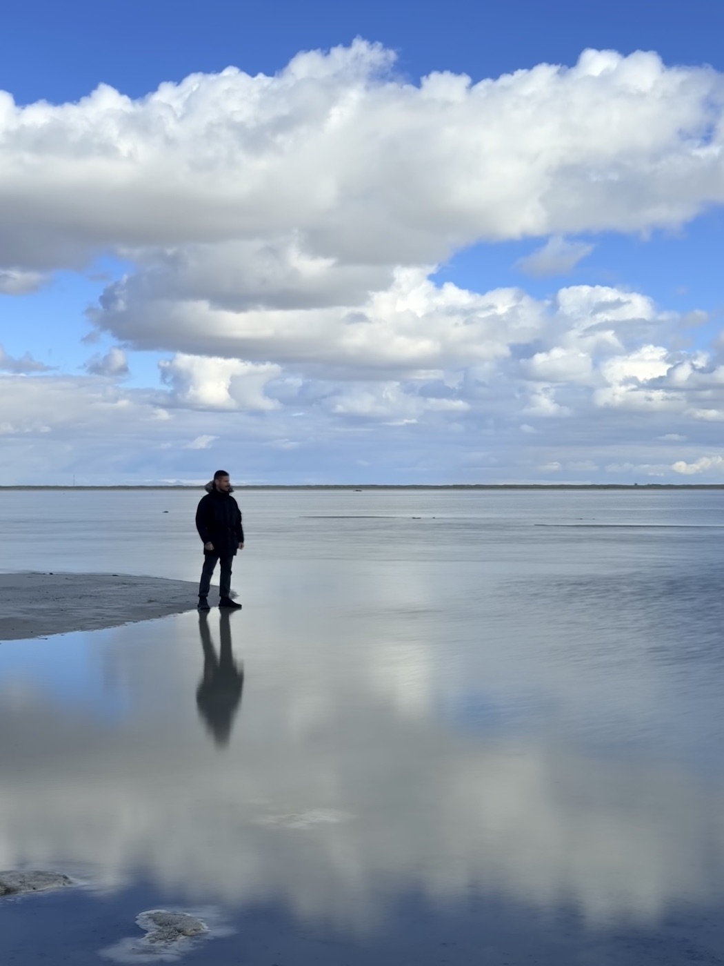 Victor standing on a tidal flat, sky mirrored in the wet sand